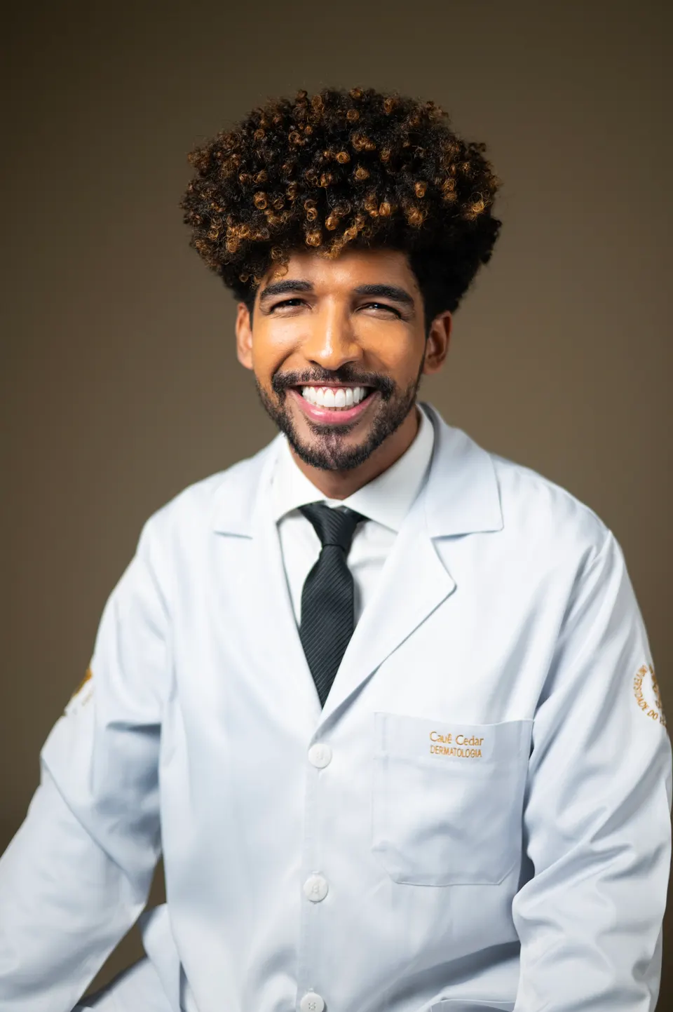 Médico de jaleco branco e gravata preta, sorrindo em retrato profissional