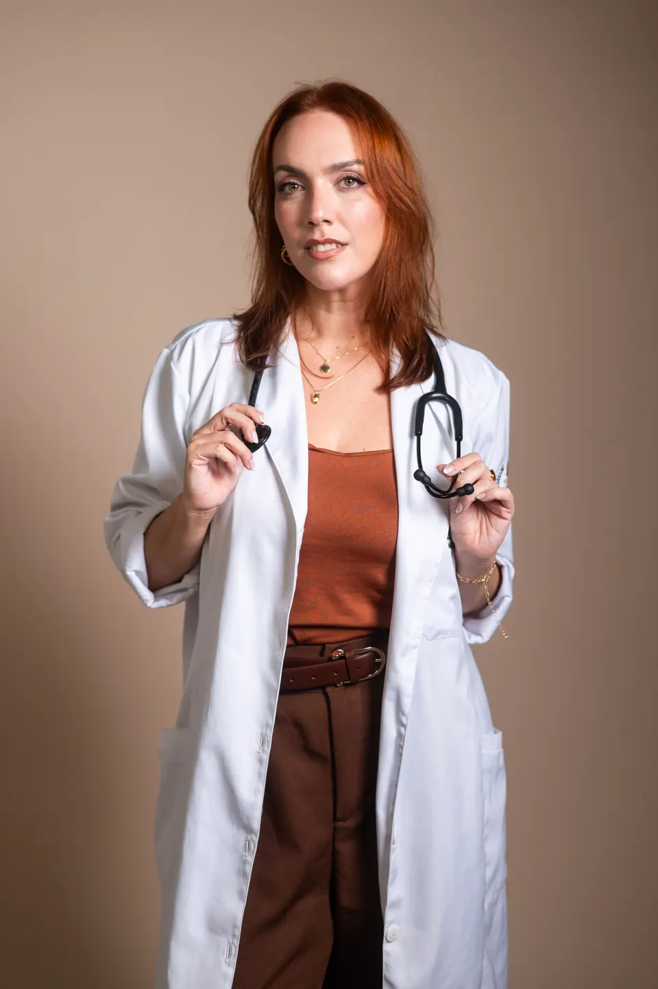 Médica ruiva de jaleco branco segurando o estetoscópio, em retrato profissional